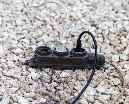 Extension cord with socket and plugs on stone rubble.