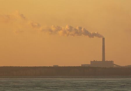 Industrial smoke from a chimney against the backdrop of the dawn of the sun.