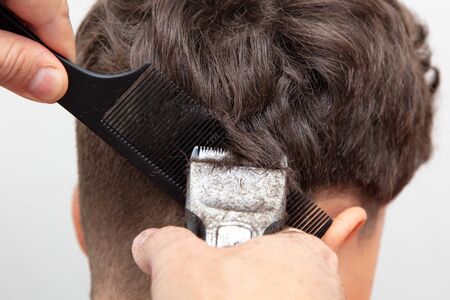 The hairdresser cuts the hair of a boy with a machine.