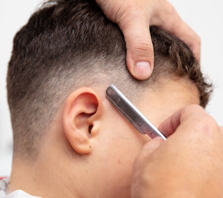 The hairdresser cuts the boy's hair with a razor.の写真素材