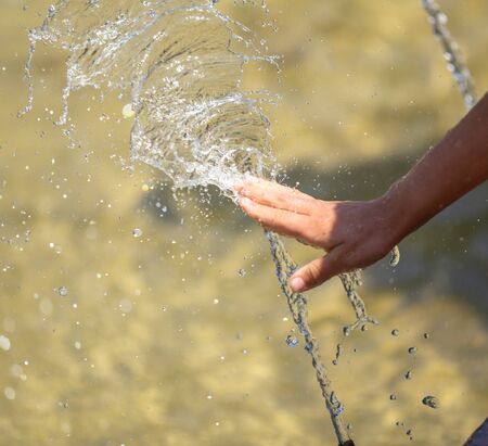 Hand of a girl in the spray of water of the fountain in the summer.の写真素材