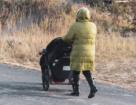 A girl in a jacket is walking with a stroller along the road.