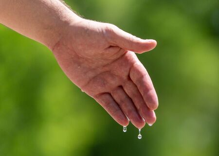 Hand of a man in the spray of water of the fountain in the summer.の写真素材