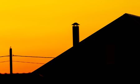 Silhouette of a chimney on the roof of a house against the backdrop of a sunset.の写真素材