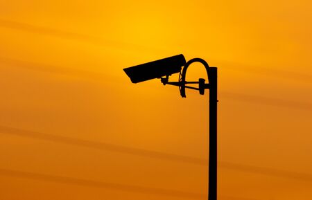 Silhouette of a cctv camera on a fence against a sunset.の写真素材