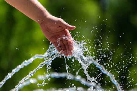 Hand of a man in the spray of water of the fountain in the summer.の写真素材