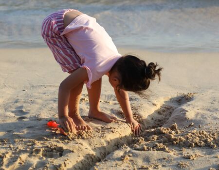 A girl plays in the sand on the seashore.の写真素材