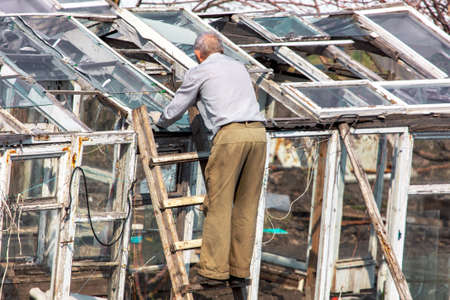 The old man on the stairs repairs the greenhouse in the country.