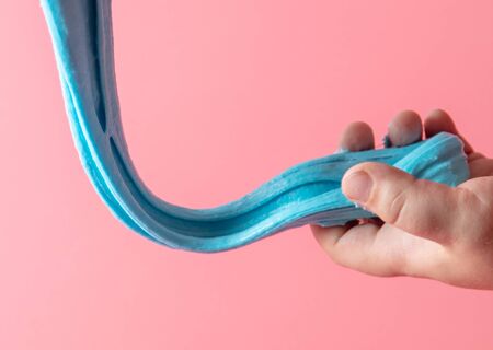 The boy is playing with a blue slime in his hands. Isolated on pink background.