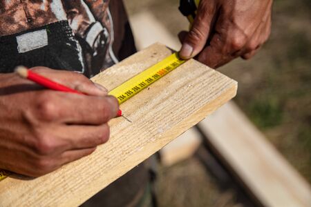 A worker measures a wooden workpiece with a meter. Building a house.の写真素材