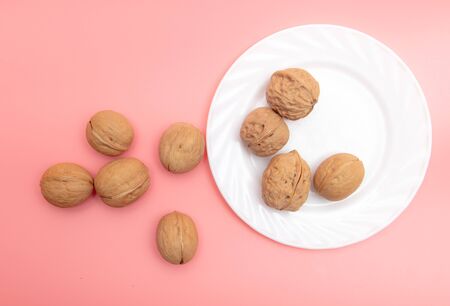 Walnuts in a white plate on a pink background.