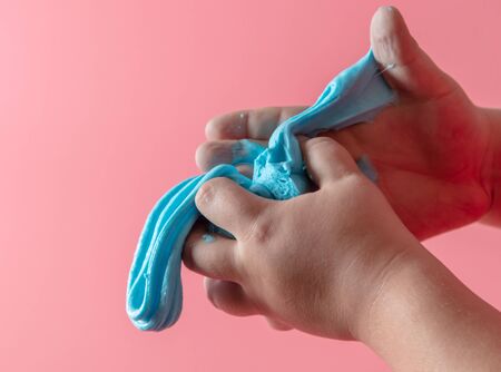 The boy is playing with a blue slime in his hands. Isolated on pink background.の写真素材