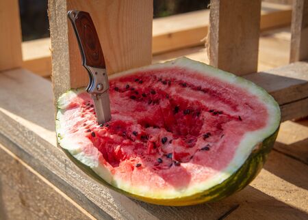 Knife in a red watermelon on wooden boards.の写真素材