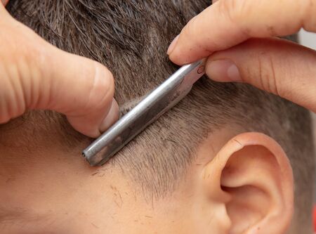 The hairdresser cuts the boy's hair with a razor.