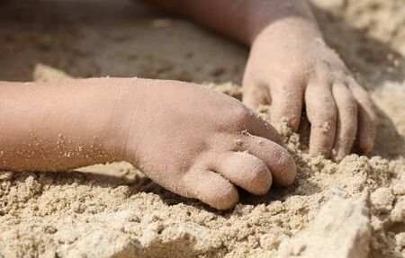 A boy plays with his hands in the sand of a beach. Holiday at the resortの写真素材
