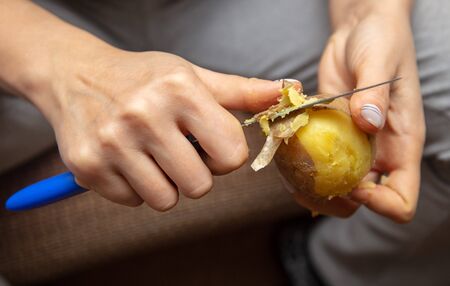 Girl peeling boiled potatoes with a knife. Cooking foodの写真素材