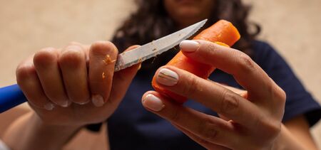 Girl peeling boiled carrots with a knife. Cooking foodの写真素材