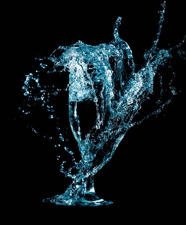 Splashes and drops of blue water in a glass are isolated on a black background.の写真素材