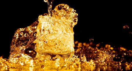 Splashes and drops of golden water in a glass are isolated on a black background.の写真素材