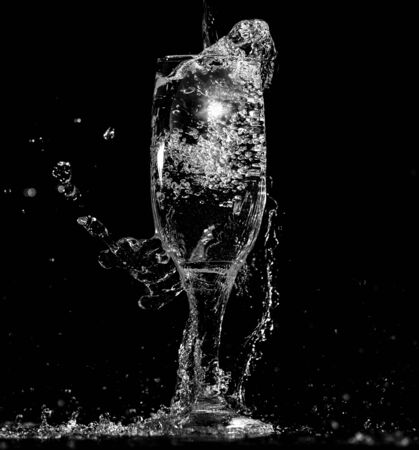 Splashes and drops of water in a glass are isolated on a black background.の写真素材