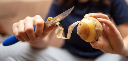 Girl peeling boiled potatoes with a knife. Cooking foodの写真素材