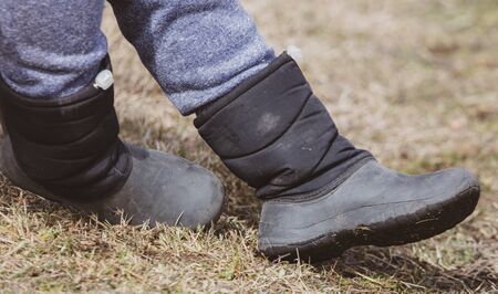 Boots on the feet of a boy on the grass in early spring.