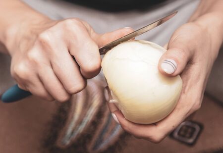 Girl peeling onions with a knife. Cooking food