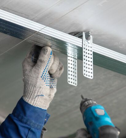 Worker fastens a metal profile to the ceiling. Repair of a room in the house.の写真素材