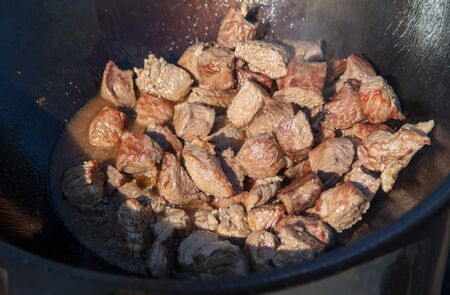 The meat is fried in oil on a cast-iron cauldron. The dish is cooked at the stakeの写真素材