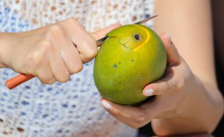 Girl cuts a mango with a knife on nature. Fruit in the tropics.