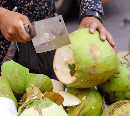 Coconut is cut with a knife for drinking milk. Market on a city streetの写真素材