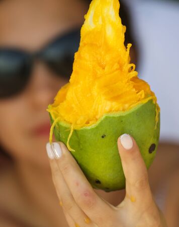 Sliced mango fruit in the girlâs hand in the park.の写真素材