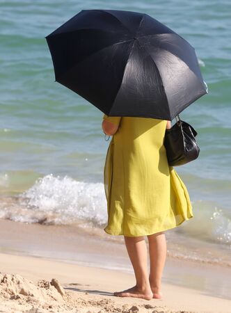 Woman with umbrella in hand on the seashore. Sun protectionの写真素材