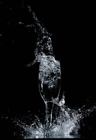 Splashes and drops of water in a glass are isolated on a black background.の写真素材