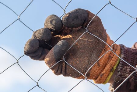 A man sets his hands a metal mesh on the fence.の写真素材