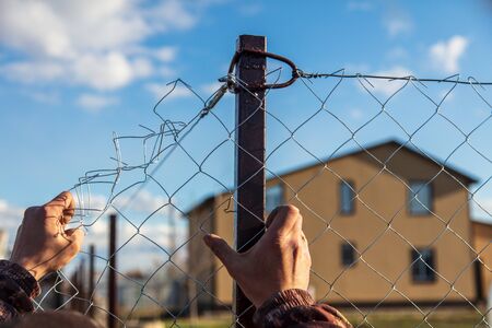 A man sets his hands a metal mesh on the fence.の写真素材