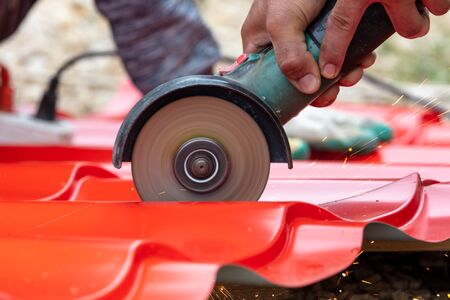 A worker cuts a red metal tile for a house roof.の写真素材