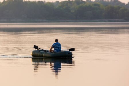 A man floats in a boat on the lake at sunset.