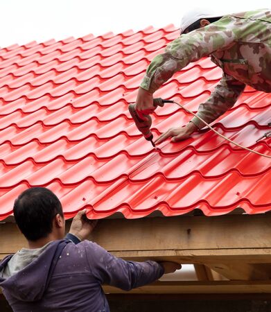 Workers install red metal tiles on the roof of the house.の写真素材