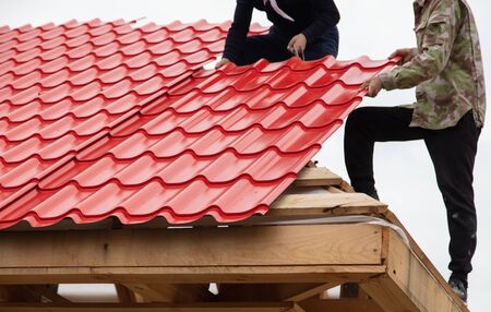 Workers install red metal tiles on the roof of the house.