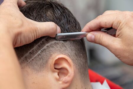 The hairdresser cuts the boy's hair with a razor.の写真素材