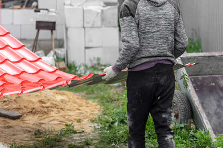 Workers install red metal tiles on the roof of the house.の写真素材