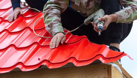 Workers install red metal tiles on the roof of the house.の写真素材