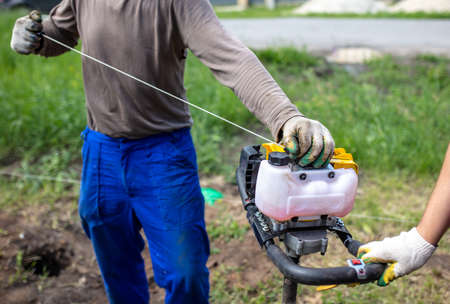 A worker is drilling soil for a gate on a fence. Starts the unit motorの写真素材