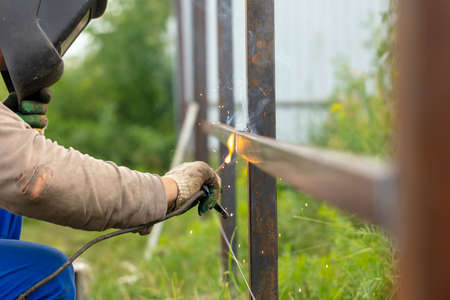Worker installs a metal fence in the summer. Welding