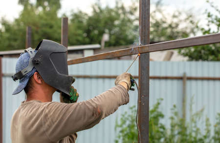Worker installs a metal fence in the summer. Welding