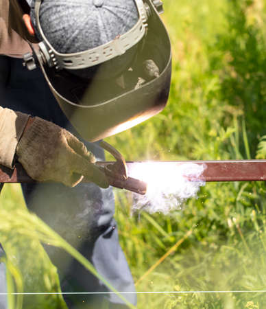Worker installs a metal fence in the summer. Welding