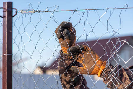 A man sets his hands a metal mesh on the fence.の写真素材