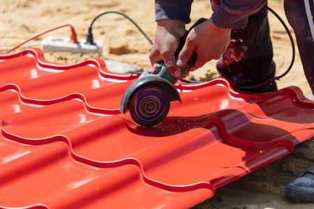 A worker cuts a red metal tile for a house roof.の写真素材