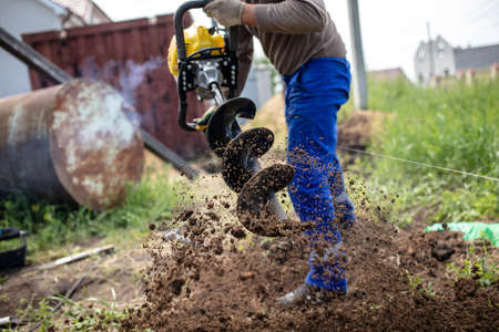 A worker is drilling soil for a gate on a fence.の写真素材
